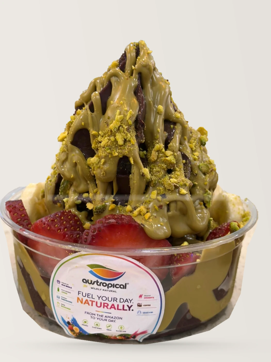 An açaí bowl under pistachio sauce and crushed pistachio, with strawberries, on the café counter.